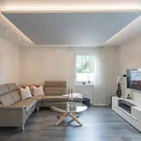 Modernes Wohnzimmer mit grauem Sofa, Glastisch, TV-Wand und stilvoller Dekoration.